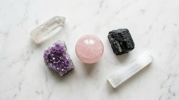 Five beginner healing crystals arranged on white marble: clear quartz, amethyst, rose quartz, black tourmaline, and selenite