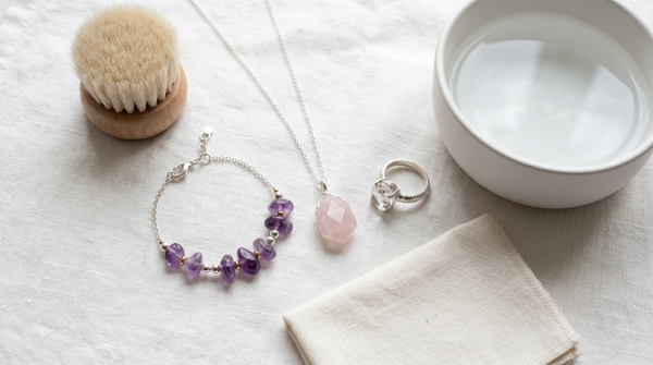 Flat lay of crystal gemstone jewelry pieces with a soft brush, bowl of water, and polishing cloth for crystal care