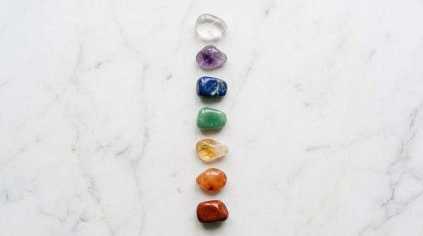 Seven chakra healing crystals arranged vertically on white marble surface