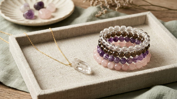 Crystal pendant and polished crystal bracelets arranged on a neutral linen jewelry tray